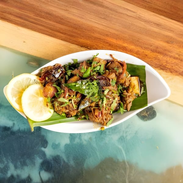 Indian chicken dish with herbs and lemon slices, served on a banana leaf in a white bowl.