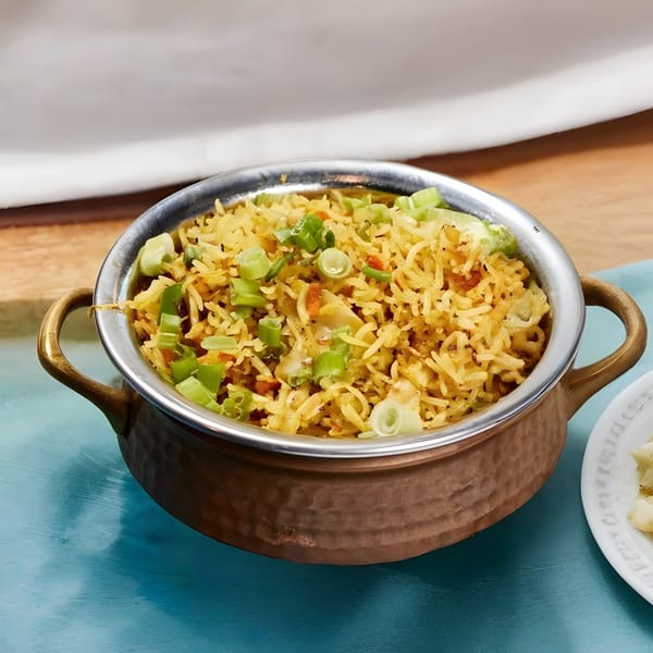 Indian fried rice with vegetables and green onions in a copper bowl on a blue surface.