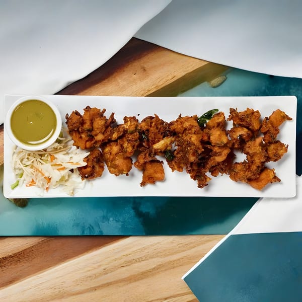 Crispy fried chicken pakora with green chutney and shredded cabbage salad on a white plate.