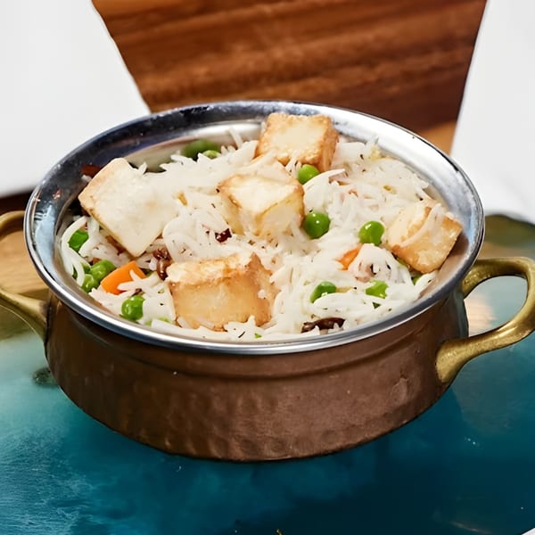 Indian paneer pulao with rice, peas, carrots, and paneer cubes in a copper pot.