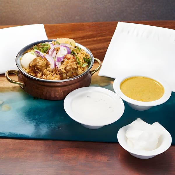 Indian biryani in a copper pot with hard-boiled eggs, red onions, and sides of sauces.